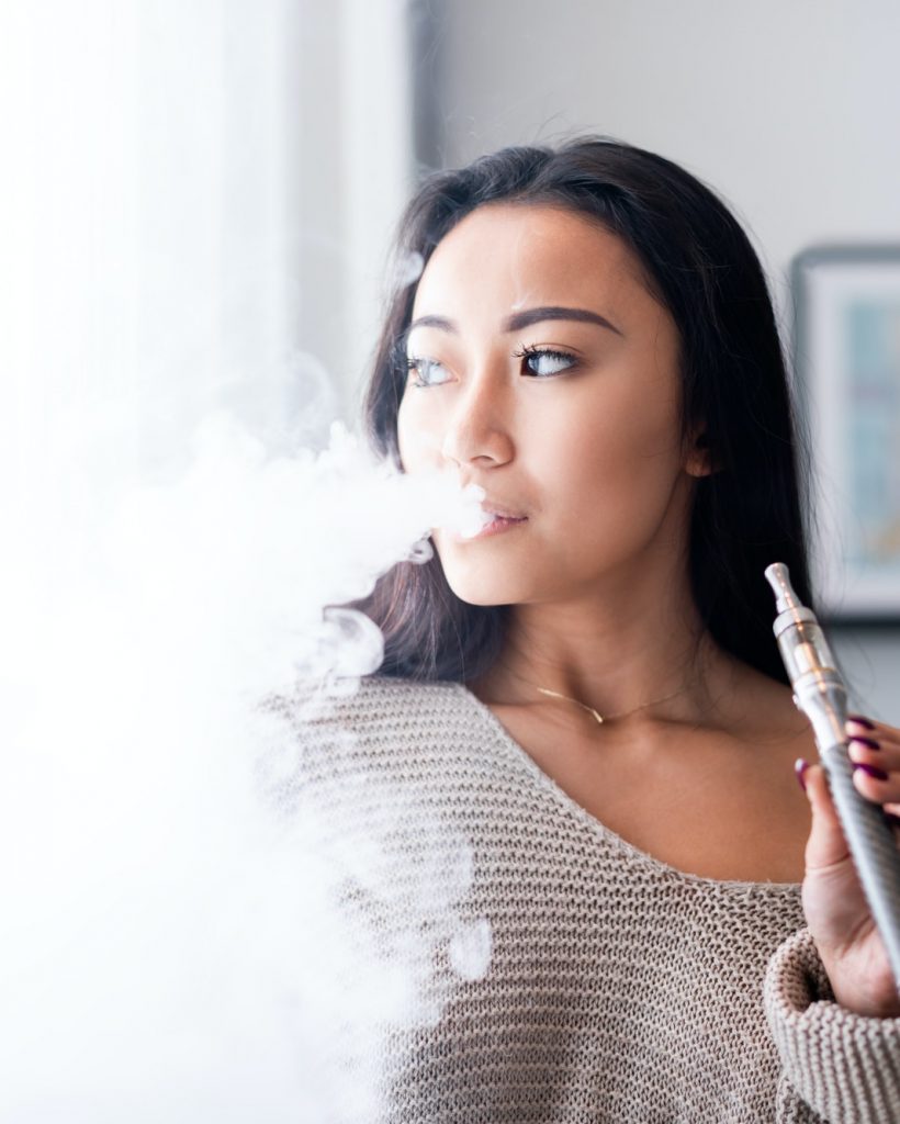 Casual asian woman vaping electronic cigarette at home