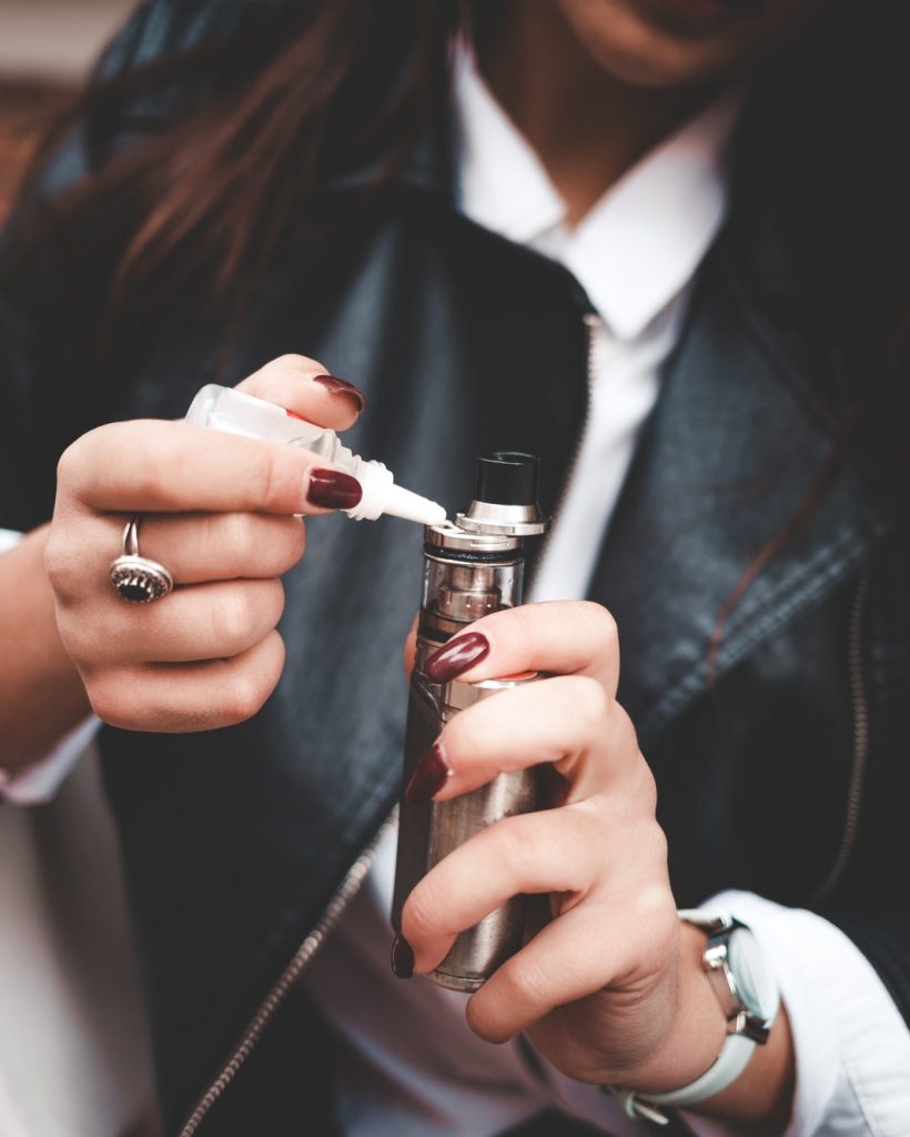 Woman refills liquid in e-cigarette closeup. Girl refills liquid in vape. Electronic cigarette